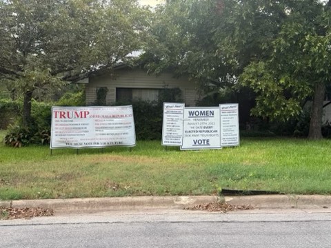 Three campaign signs stand on a grassy lawn in front.