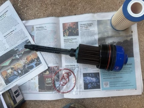 Newspaper with printed articles, blue and black mechanical parts, and red O-rings laid on a carpeted surface.
