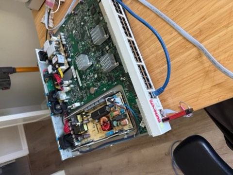 Close-up of a Fortigate 140E device with internal circuit board, blue and gray cables, and red connector visible on a wooden surface.