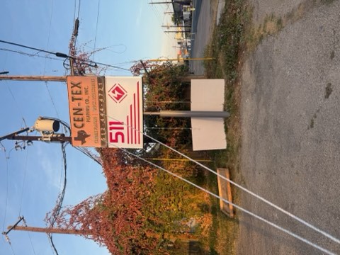 A signpost with 'CEN-TEX Parking Co. Inc.' and '511' on a pole, near a road with utility poles and autumn foliage.