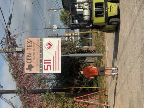 A forklift lifts a sign near a road with a person standing nearby.
