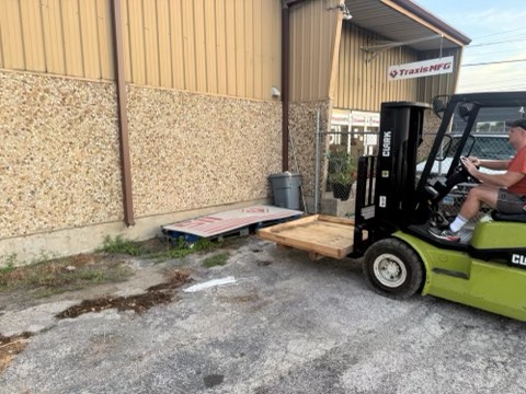 Green forklift with wooden pallet on lift, near industrial building with corrugated metal and stone wall.