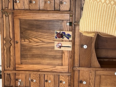 Wooden furniture with striped wood grain, two small rectangular labels with designs, and knobs, with a yellow woven item partially visible on the right.