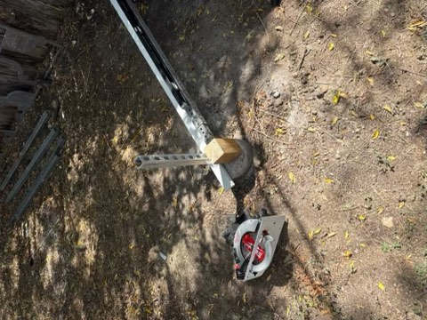 Metal rail, wooden post, and miter saw on dirt ground with scattered leaves and debris.
