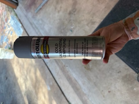 Hand holding a Rust-Oleum Professional Cold Galvanizing Compound spray can for metal repair.